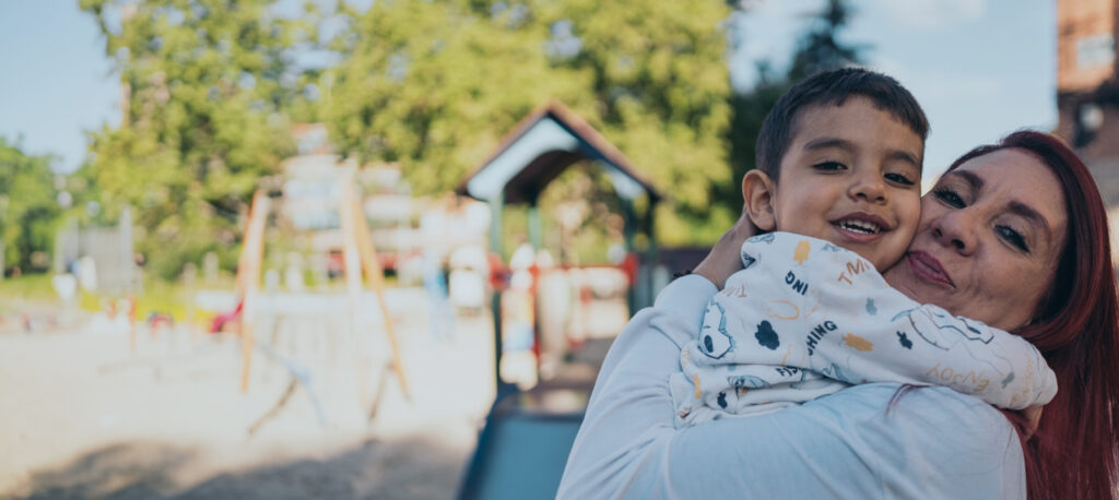 A mother holding a smiling child at a playground.