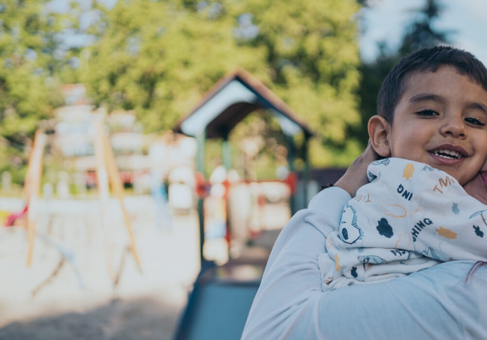 A mother holding a smiling child at a playground.