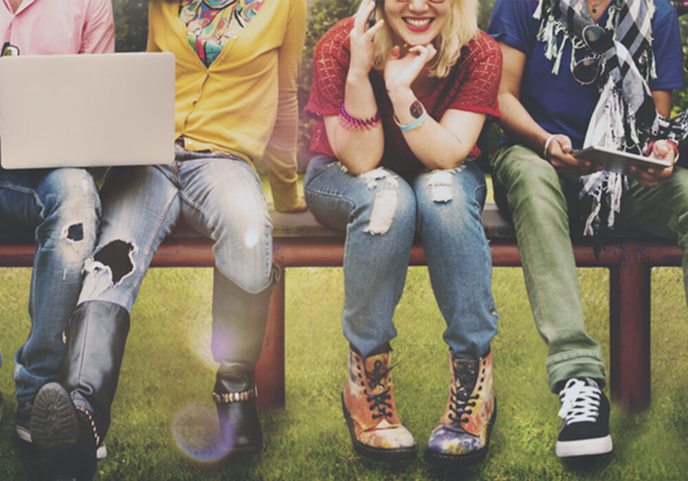 Four teenagers sitting on a bench together. The camera frame is putting emphasis on their outfits with different colors and shoe types.